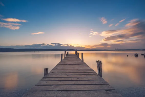 A wooden dock leading out to a lake at dusk.
